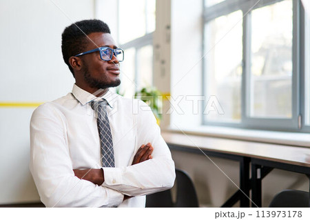Confident African corporate pro stands in modern office, arms crossed, looking away optimistically. Visionary leader in formal attire reflects diversity in workplace, success, leadership, growth. Confident African corporate pro stands in modern office, arms crossed, looking away optimistically. Visionary leader in formal attire reflects diversity in workplace, success, leadership, growth. 113973178