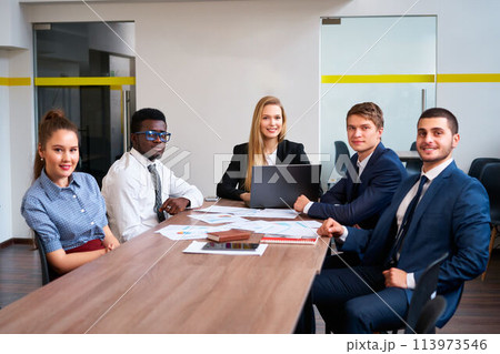 Multiracial corporate team in meeting at office desk, engaged in strategy session with laptop, papers, reflecting teamwork, innovation in modern work environment with focus on diversity and inclusion. Multiracial corporate team in meeting at office desk, engaged in strategy session with laptop, papers, reflecting teamwork, innovation in modern work environment with focus on diversity and inclusion. 113973546