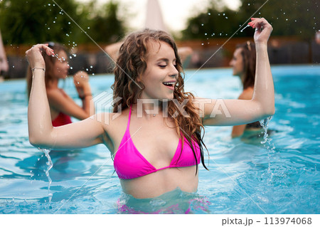 Pretty woman in bikini hanging out with friends at pool party in beach club. Curly cute girl in swimwear enjoy summer. People have fun swimming in water in luxury private villa swimming pool. Pretty woman in bikini hanging out with friends at pool party in beach club. Curly cute girl in swimwear enjoy summer. People have fun swimming in water in luxury private villa swimming pool. 113974068