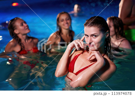 Pretty woman in red bikini hanging out with friends at night pool party in beach club. Nice girl in hot swimwear enjoy summer. People have fun swimming at water in luxury private villa swimming pool. Pretty woman in red bikini hanging out with friends at night pool party in beach club. Nice girl in hot swimwear enjoy summer. People have fun swimming at water in luxury private villa swimming pool. 113974078