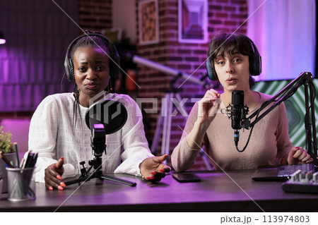 African american content creator and cohost during online show in rgb lights studio, shooting vlog using professional microphones. Vloggers chatting with audience during streaming service broadcast African american content creator and cohost during online show in rgb lights studio, shooting vlog using professional microphones. Vloggers chatting with audience during streaming service broadcast 113974803