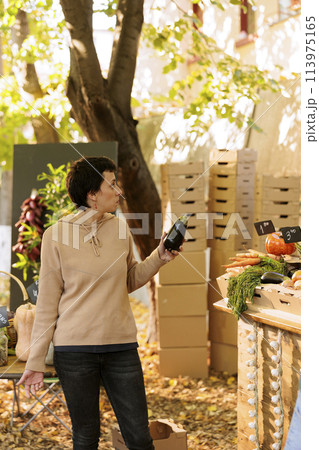 Young female customer with an eggplant in hand, purchasing locally grown colorful fresh natural produce. Woman shopper standing at farmers market booth, ready to buy freshly harvested veggie. Young female customer with an eggplant in hand, purchasing locally grown colorful fresh natural produce. Woman shopper standing at farmers market booth, ready to buy freshly harvested veggie. 113975165