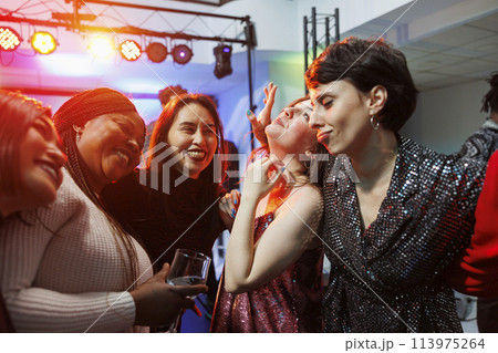 Cheerful smiling women drinking alcohol, hugging and partying together in nightclub. Carefree diverse girlfriends holding beverage glasses, laughing and having fun in club 113975264