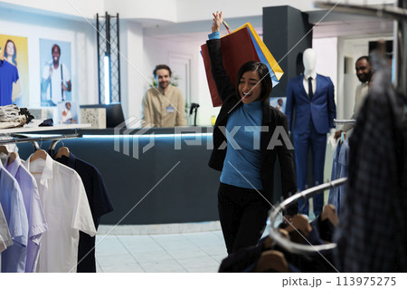 Happy woman making dance moves with shopping bags after buying garment in clothing store. Fashion boutique smiling asian customer raising hand with paper packages of purchases Happy woman making dance moves with shopping bags after buying garment in clothing store. Fashion boutique smiling asian customer raising hand with paper packages of purchases 113975275