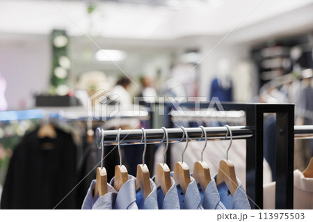 Male formal shirts hanging on metal rack in shopping center boutique. Stylish menswear brand from new collection showcasing for clients on hangers in clothing store with blurred background 113975503