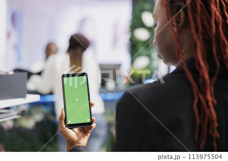 African american woman using smartphone with green screen while shopping for clothes in mall. Boutique buyer holding mobile phone with empty chroma key display for copy space 113975504