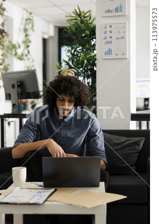 Arab executive manager working at start up project development in business office. Young businessman sitting on couch at workspace and checking marketing research on laptop 113975573