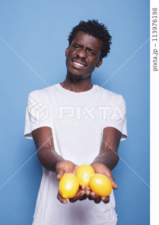 African american person holding lemons for healthy vegetarian diet. Man presenting yellow citrus fruits in hands for natural nutrition with vitamins. Adult showing fresh juicy fruits to camera. African american person holding lemons for healthy vegetarian diet. Man presenting yellow citrus fruits in hands for natural nutrition with vitamins. Adult showing fresh juicy fruits to camera. 113976198