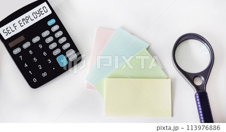 Self-employed word on a calculator, next to a magnifying glass and stickers on a white background Self-employed word on a calculator, next to a magnifying glass and stickers on a white background 113976886