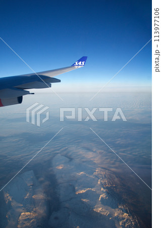 COPENHAGEN, DENMARK - 24 NOV 2018: Aeroplane window view with plane wing flying over the icebergs of Greenland at sunset with aerial perspective 113977106