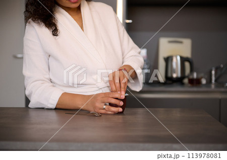 Close-up young woman in white bathrobe, standing at kitchen table at home, having a breakfast Close-up young woman in white bathrobe, standing at kitchen table at home, having a breakfast 113978081