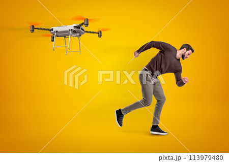 Young man in casual clothes running from camera drone that chases him on amber background. 113979480