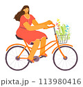 Woman cycling leisurely, enjoying sunny day. Female cyclist wears casual dress, rides orange bike, carries flowers basket. Smiling lady curly hair, glasses pedals through leisure scene 113980416