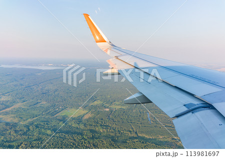 View of airplane wing, blue skies and green land during landing. Airplane window view. View of airplane wing, blue skies and green land during landing. Airplane window view. 113981697