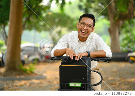 Cheerful Asian male office worker with bicycle in city park. Active lifestyle and transport concept 113982279