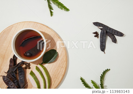 A bowl of brown liquid with black locust pod soaked in, extracted from locust fruit helps restore damaged, tangled, and broken hair. Top view, blank space A bowl of brown liquid with black locust pod soaked in, extracted from locust fruit helps restore damaged, tangled, and broken hair. Top view, blank space 113983143