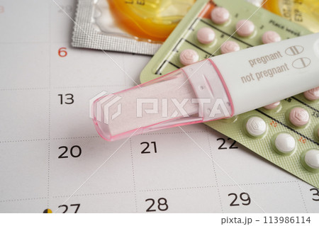 Pregnancy test with birth control pills and condom for female on calendar, ovulation day. 113986114