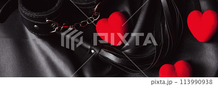 set of BDSM sex toys with handcuffs, whip flogger with red hearts for submission and domination on black background. Gift for Valentine's day 113990938