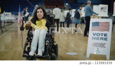 Woman with SMA smiles and looks at camera in polling station 113991439