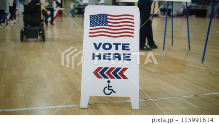 Vote here sign on floor. Woman in electric wheelchair comes to vote Vote here sign on floor. Woman in electric wheelchair comes to vote 113991614