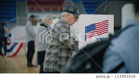 Male voter with bulletin in hands comes to voting booth Male voter with bulletin in hands comes to voting booth 113991616