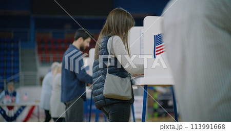 Caucasian female voter comes with bulletin to voting booth Caucasian female voter comes with bulletin to voting booth 113991668
