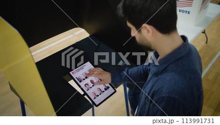 Caucasian man makes choice and votes in voting booth using tablet computer Caucasian man makes choice and votes in voting booth using tablet computer 113991731