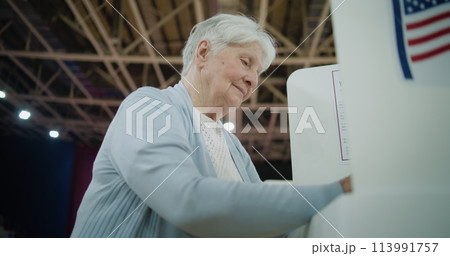 Elderly female voter stands at voting booth 113991757