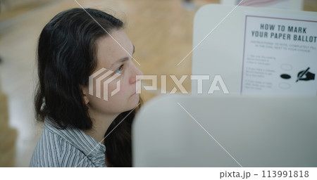 Female voter stands at voting booth in polling station Female voter stands at voting booth in polling station 113991818
