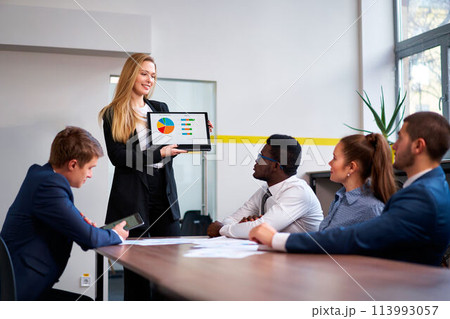 Female CEO presents colorful chart on laptop to multiethnic colleagues during meeting. Male, female employees engage in strategy discussion, African, Caucasian, Asian members collaborate. Female CEO presents colorful chart on laptop to multiethnic colleagues during meeting. Male, female employees engage in strategy discussion, African, Caucasian, Asian members collaborate. 113993057