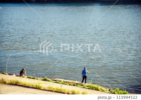 fisherman fishing with fishing rods in city river. two persons catch fish on summer evening 113994522