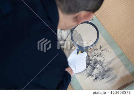 古い掛け軸の鑑定をしている男性作業員 113998578