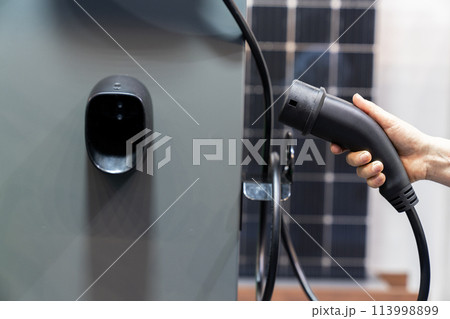 Hand with electric vehicles charging plug on a background of solar panel 113998899