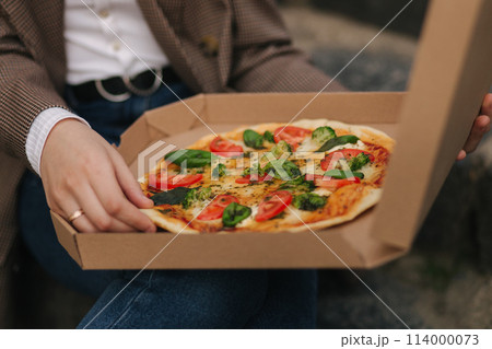 Close up of Woman open pizza box outdoors. Female hold open pizza box and smells appetizing Close up of Woman open pizza box outdoors. Female hold open pizza box and smells appetizing 114000073