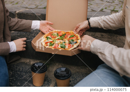 Close-up of Couple grab slices of pizza from box at the outdoor. Man and woman hands taking pizza. Vegan pizza with fresh tomatoes basil and broccoli. Lactose and gluten free 114000075