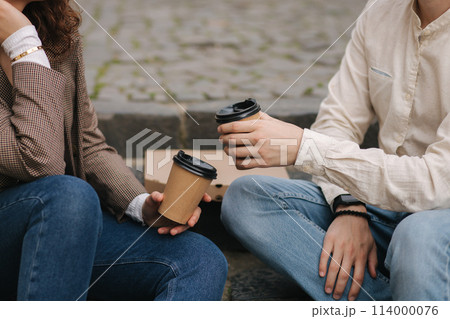 Smiling love couple sitting on the stairs outdoor and hold cup of coffee. Middle selection Smiling love couple sitting on the stairs outdoor and hold cup of coffee. Middle selection 114000076