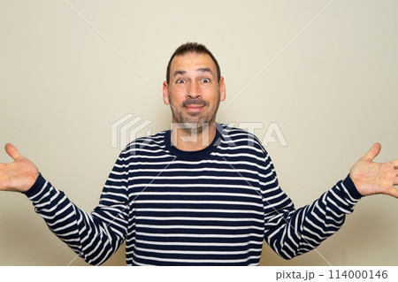 Hispanic man with beard in his 40s wearing a striped sweater clueless and confused with open arms, no idea concept. Isolated on beige studio background. 114000146