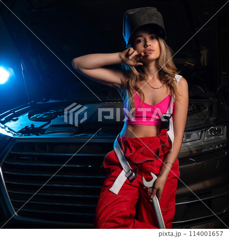 a beautiful girl in a uniform repairs a car at a car service station a beautiful girl in a uniform repairs a car at a car service station 114001657