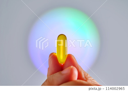 Capsule of omega 3 in hand against the background of a glowing circle. Capsule of omega 3 in hand against the background of a glowing circle. 114002965