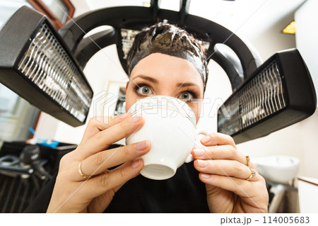 Woman in hairdresser drinking coffee under machine Woman in hairdresser drinking coffee under machine 114005683