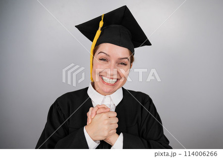 Caucasian woman in graduate gown dreamily holds her hands on her chest. Caucasian woman in graduate gown dreamily holds her hands on her chest. 114006266