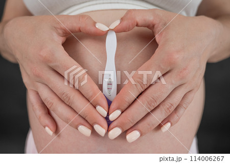 Caucasian woman holding a positive express pregnancy test against the background of her tummy. Caucasian woman holding a positive express pregnancy test against the background of her tummy. 114006267