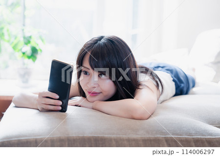 ソファでリラックスしてスマホを使う若い女性 ソファでリラックスしてスマホを使う若い女性 114006297