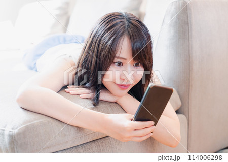 ソファでリラックスしてスマホを使う若い女性 ソファでリラックスしてスマホを使う若い女性 114006298