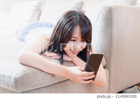 ソファでリラックスしてスマホを使う若い女性 114006300