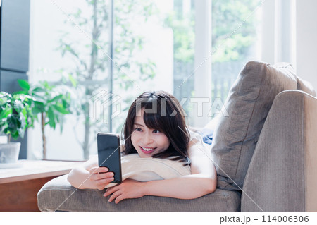 ソファでリラックスしてスマホを使う若い女性 ソファでリラックスしてスマホを使う若い女性 114006306