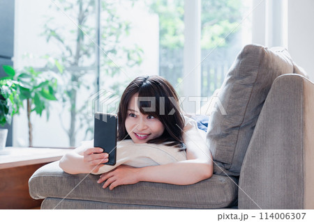 ソファでリラックスしてスマホを使う若い女性 ソファでリラックスしてスマホを使う若い女性 114006307
