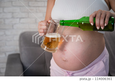 Faceless pregnant woman pouring beer into a glass.  114006361
