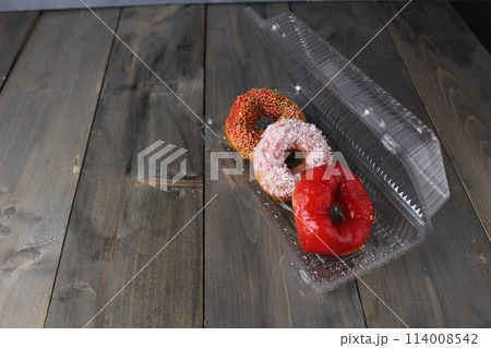 Three red donuts in a plastic box on a gray background with space for copyspace text. Donut Day Candy Delivery American Food 114008542
