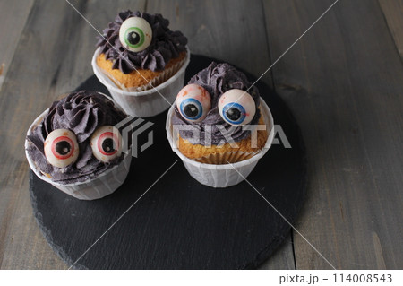 Three cupcakes with grey black cream and eyes. Halloween Holiday Preparation Concept Three cupcakes with grey black cream and eyes. Halloween Holiday Preparation Concept 114008543